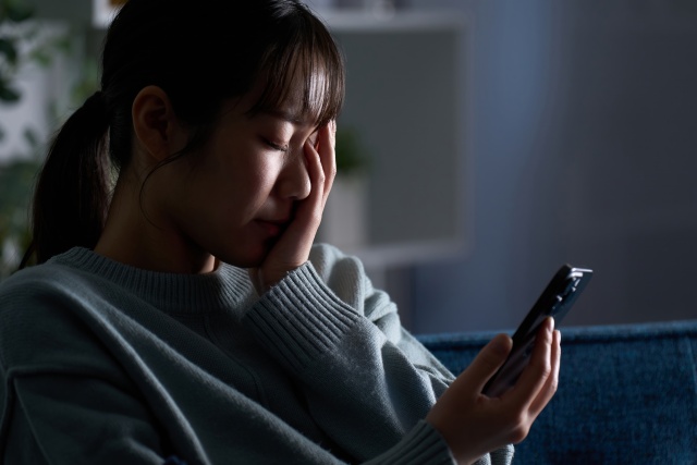 深夜にスマホを見て寝不足で疲れている様子